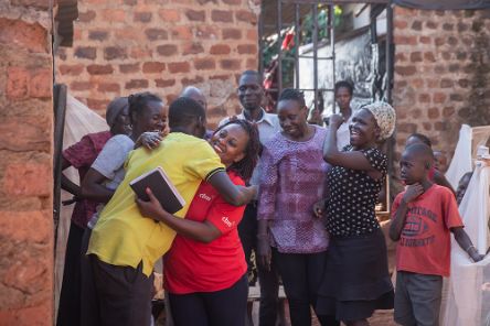 Eine Frau und ein Mann umarmen sich, weitere Frauen, Männer und Kinder stehen dabei. Die meisten lächeln.
