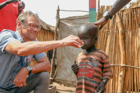 Ein Mann gibt einem Kind mit einem kleinen Becherchen etwas zu trinken.