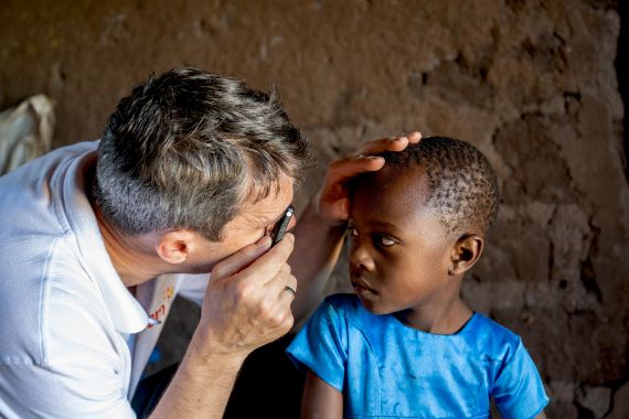 Ein Mann untersucht die Augen eines Kindes in einer Hütte.